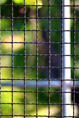 Close-up shot of a metal fence grid with blurred green background, creating an abstract pattern.