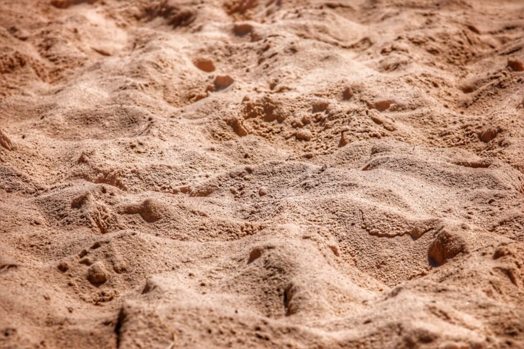 Detailed close-up of sandy beach texture under bright sunlight, showcasing natural patterns.